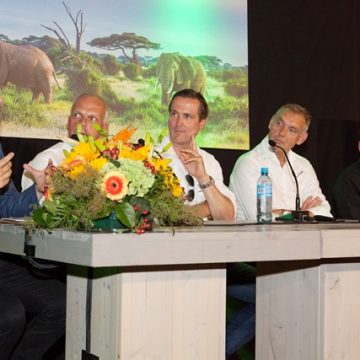 4 mannen aan een bar, met een microfoon voor hun en een grote bos bloemen